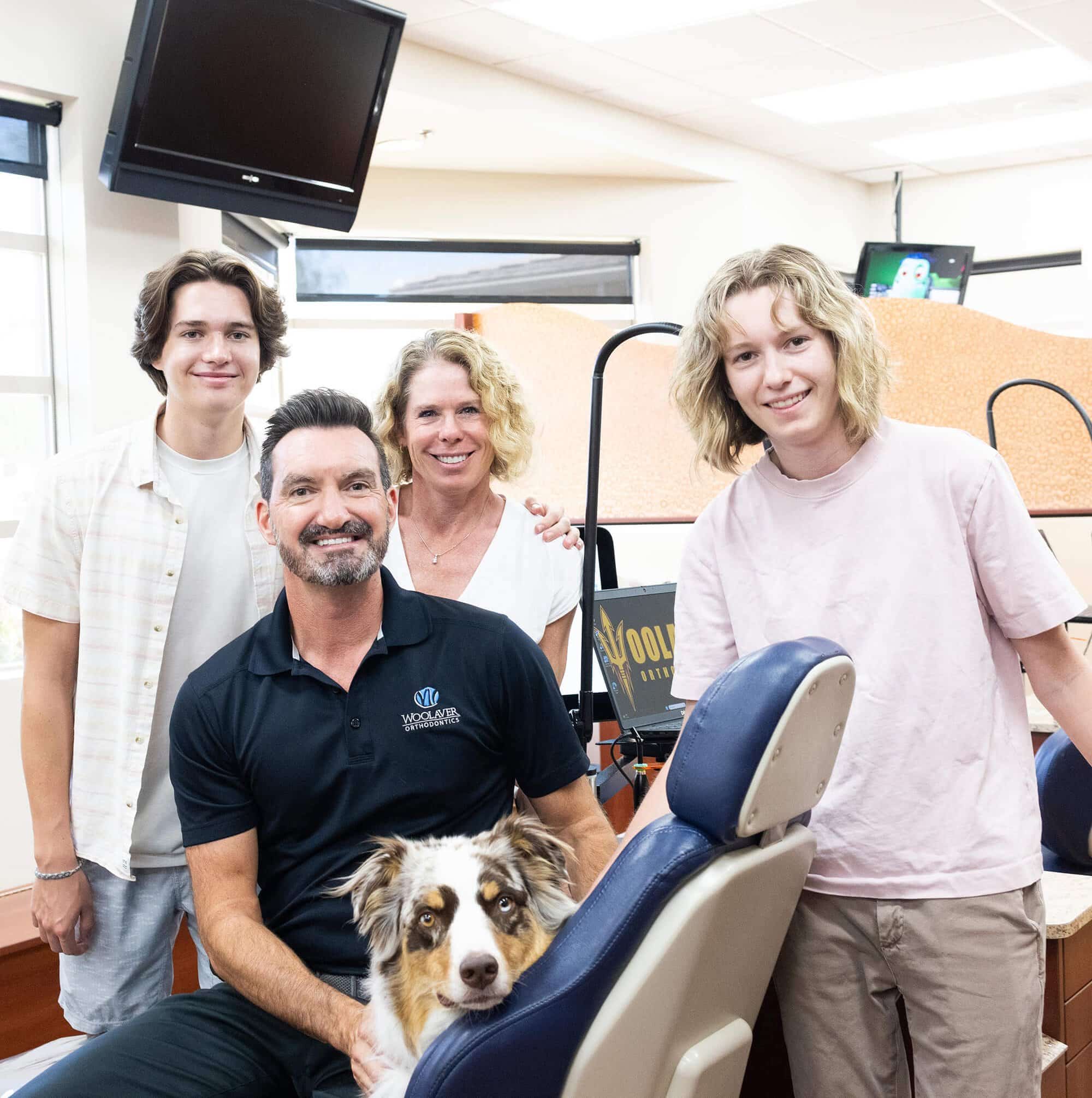 The team of four Orthodontists from Woolaver Orthodontics in Phoenix, all smiling and one of them holds a dog in his lap.